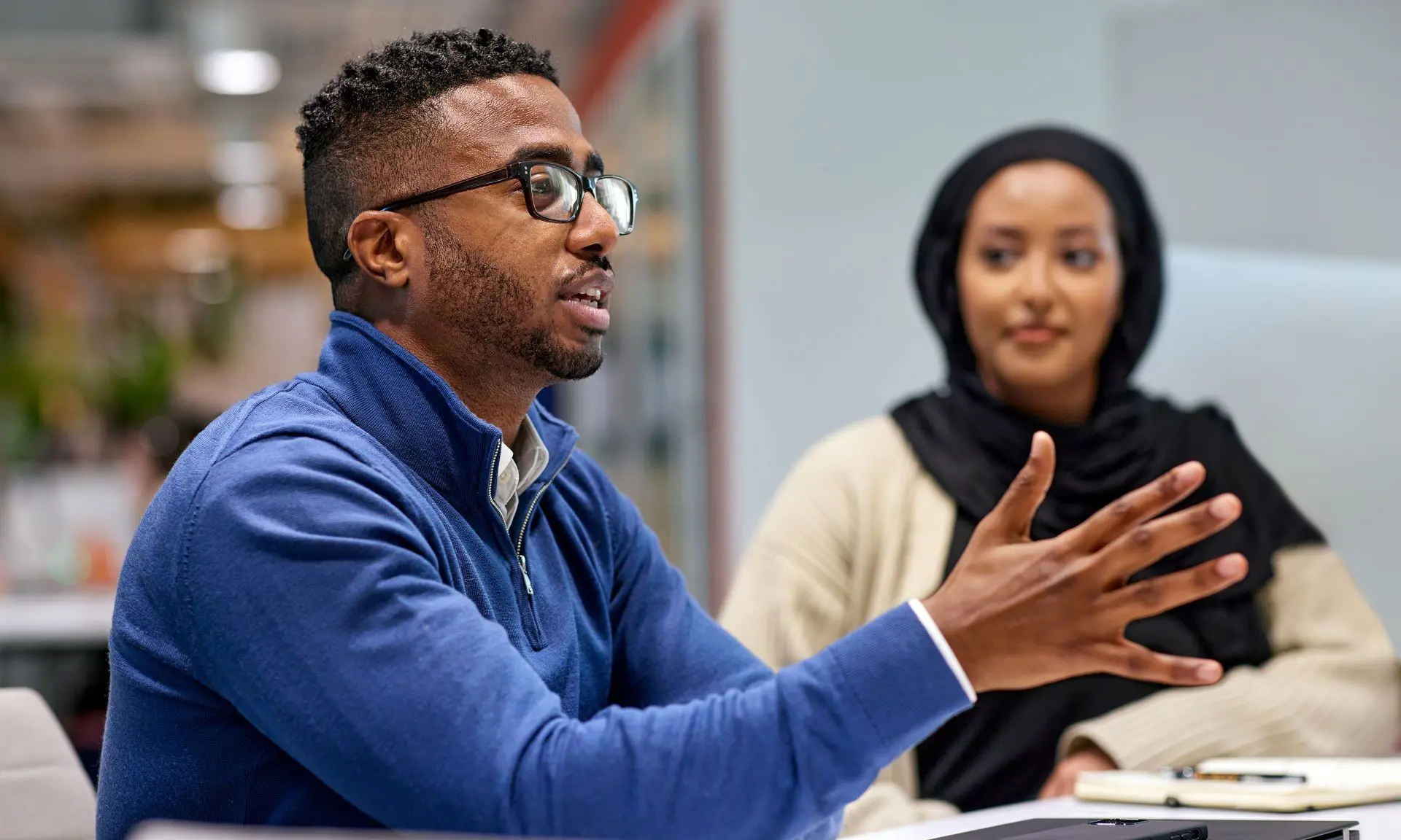 A black male employee and black female employee in the office having a discussion.