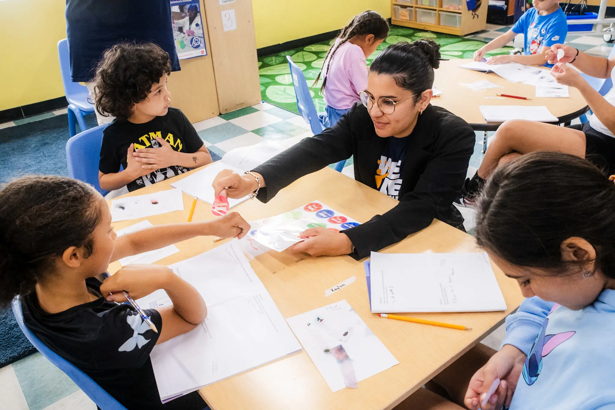 Three children at a school table with a teacher working on a worksheet