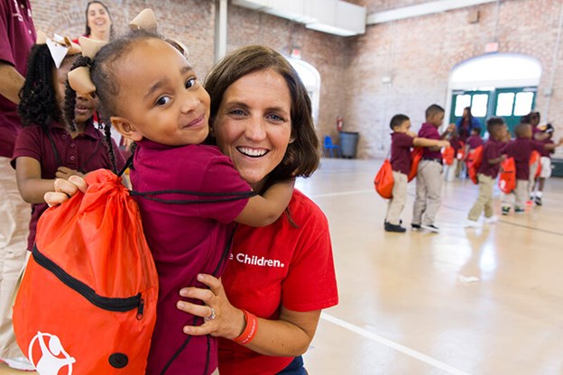 Young girl with a backpack hugging a volunteer