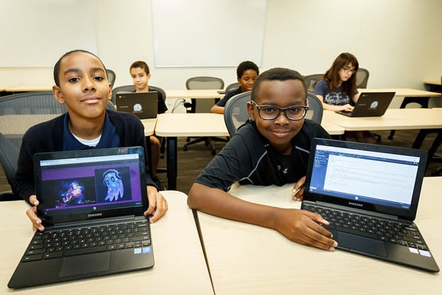 Two young boys with laptops showing the designs they made during a computer class