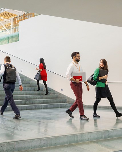Several colleagues walking in an open space near a wide stairwell 