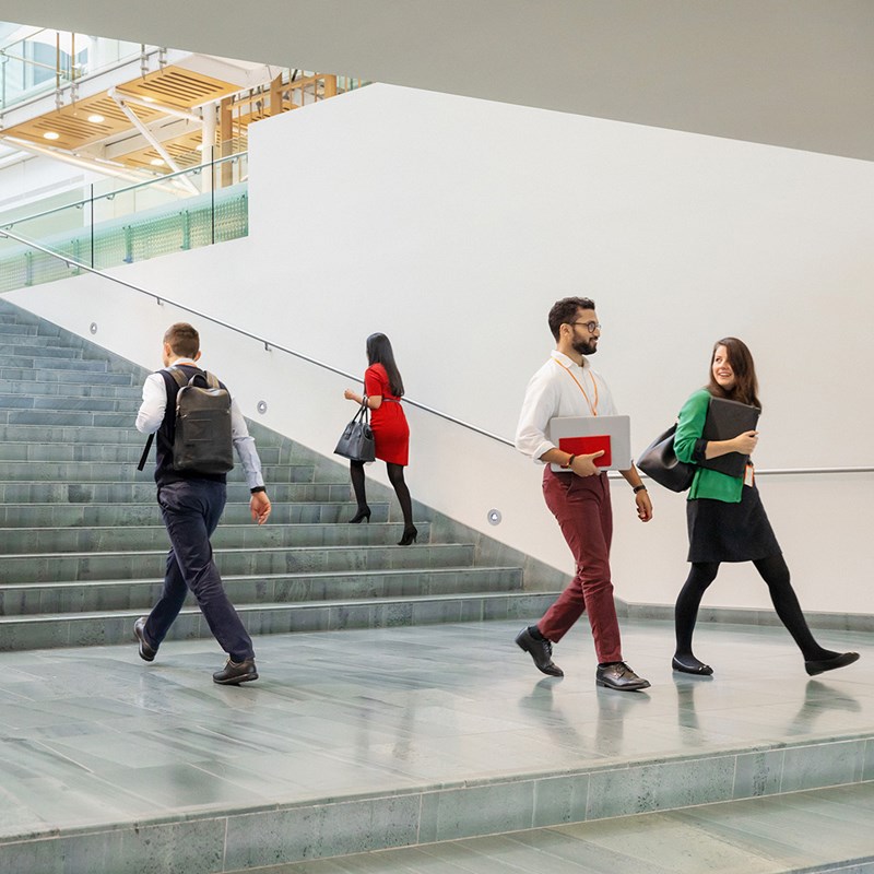 Several colleagues walking in an open space near a wide stairwell 