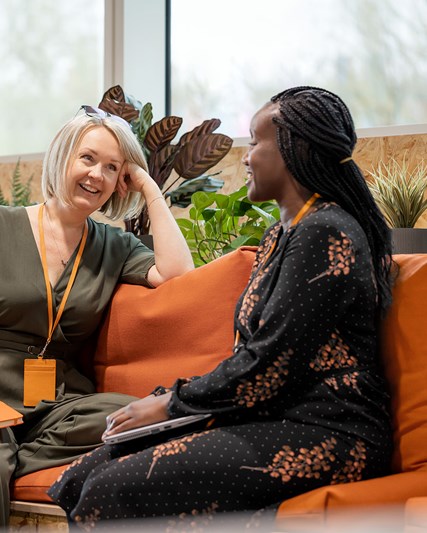 Two women chatting on an orange couch, smiling