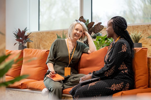 Two women chatting on an orange couch, smiling