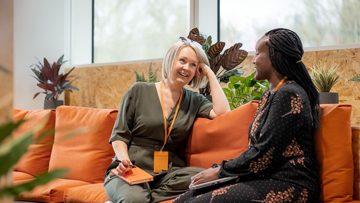 Two women chatting on an orange couch, smiling