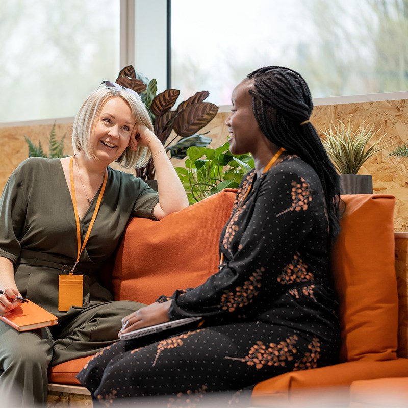 Two women chatting on an orange couch, smiling