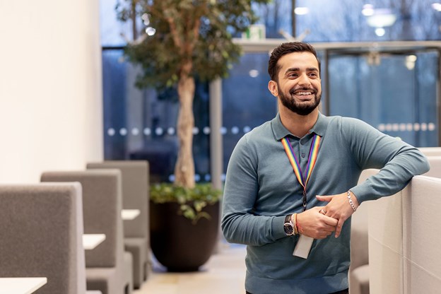 Man with beard and blue shirt smiling at camera in an office lobby 