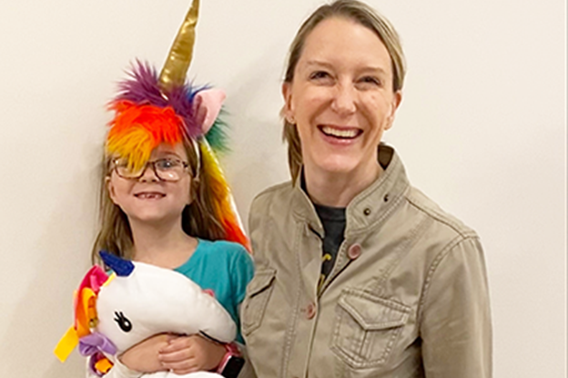 Young child in a unicorn costume standing with her mother