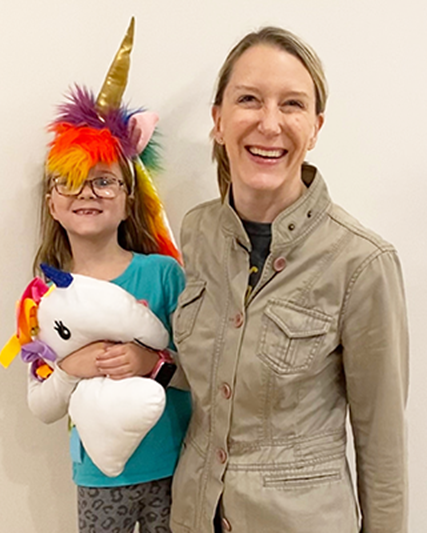 Child in a unicorn costume standing with her mother