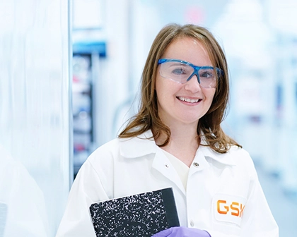 Beth in a lab coat and protective goggles looking at the camera