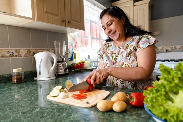 mujer latina en su cocina cortando vegétales.
