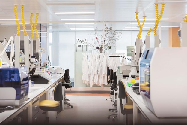 Lab desks and chairs with lab coats hanging in the background 