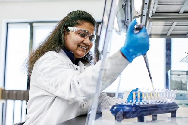 Scientist wearing goggles, white jacket, blue gloves using a pipette 